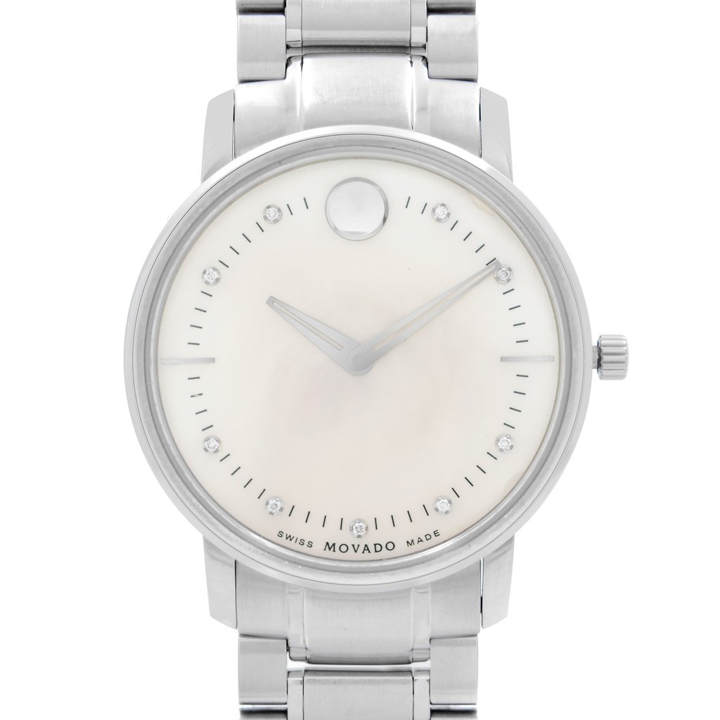 An image of a pre-owned wristwatch captured from a front close-up angle. The watch features a clean, minimalist face with a metallic band. The hands and hour markers are simple, with a distinct round emblem at the 12 o'clock position. The brand name is subtly visible at the bottom of the watch face.
