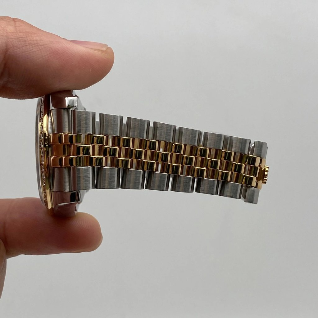 An image of a pre-owned Rolex unisex wristwatch held between fingers, viewed from the side. The watch features a gold and steel metal bracelet with a prominent date indicator. The angle shows the watch's profile and band detail, with the camera positioned close to capture the intricate design.
