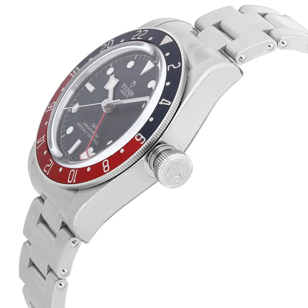An image of a TUDOR men's luxury sport wristwatch in an unworn condition, shown from a side profile view highlighting the crown. The watch features a round stainless steel case and band, with a black dial and a bi-color bezel in blue and red. The watch includes a date indicator, GMT function, and luminous hands. The angle captures the intricate details of the crown and bezel, with a close-up distance emphasizing the craftsmanship.