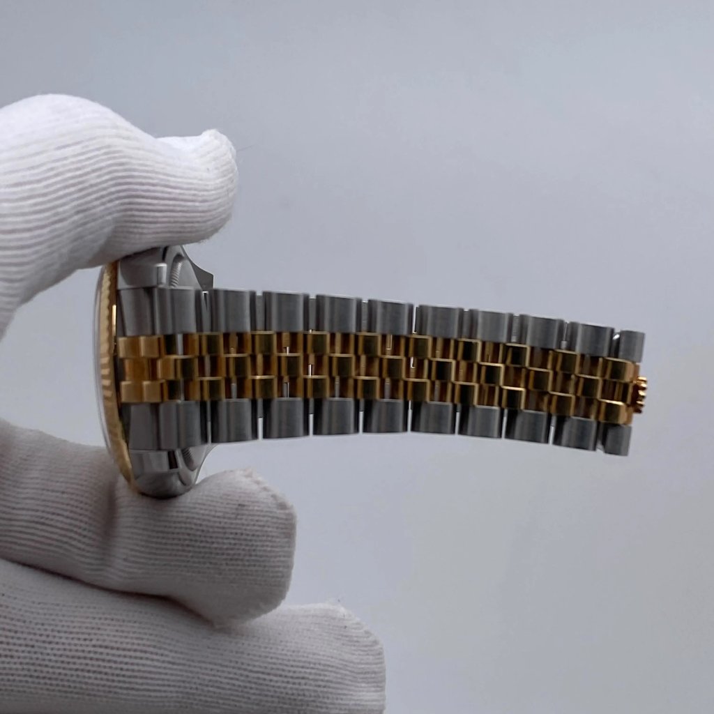 An image of a pre-owned men's Rolex wristwatch held by a gloved hand. The watch is viewed from the side, showcasing its metal bracelet with alternating gold and stainless steel links. The watch face is slightly visible from a side angle. The photograph is taken at close range, highlighting the watch's details and craftsmanship.
