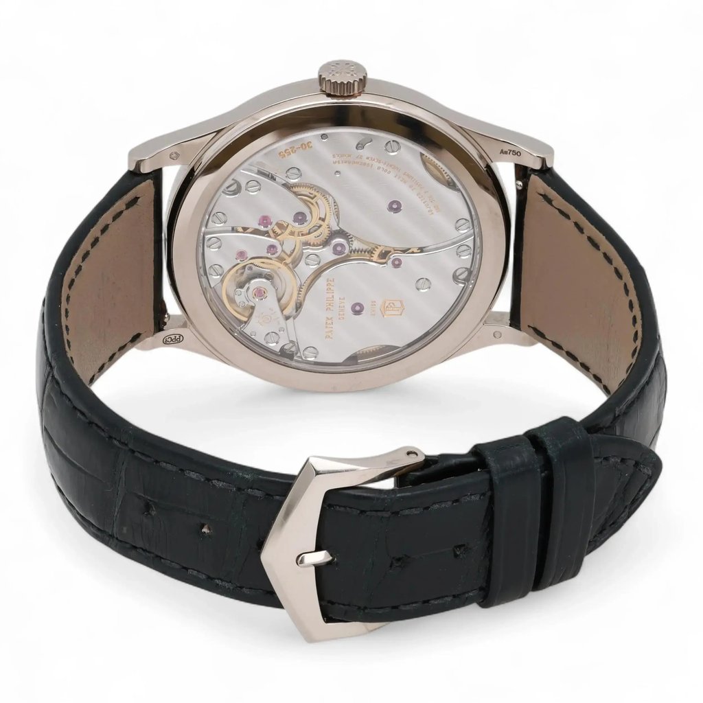 An image of a pre-owned men's Patek Philippe wristwatch captured from a slightly elevated rear angle, showcasing the intricate mechanics of the watch's movement. The watch is positioned upright with its black leather strap partially fastened and the silver buckle facing forward. The detailed gears and components are visible through the transparent case back, highlighting the craftsmanship. The photograph is taken at a close distance to emphasize the watch's design and engineering.