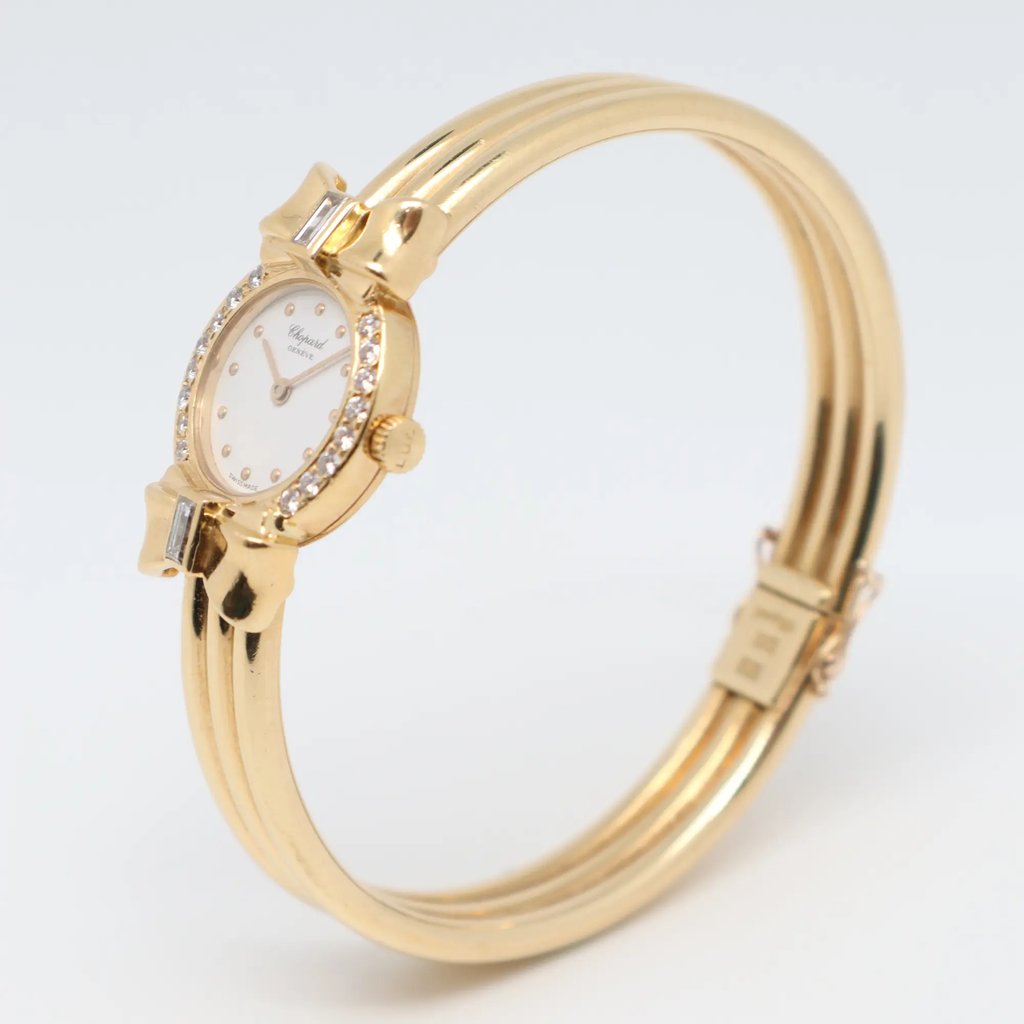 An image of a pre-owned women's Chopard wristwatch, positioned upright and viewed from a slight angle. The watch is captured at a medium distance, showcasing its yellow gold bracelet and a round face adorned with small, sparkling diamonds around the bezel. The watch face displays minimalistic hour markers and hands, emphasizing its elegant design.