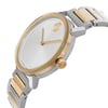 An image of a pre-owned wristwatch shown from a side profile view. The focus is on the crown, which is prominently displayed. The watch features a round face with a gold bezel and a two-tone metal strap. The angle highlights the sleek design and the contrast between the gold and silver tones.