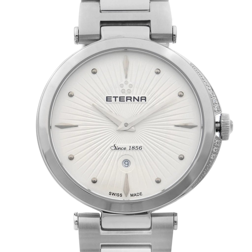 An image of a wristwatch taken from a front close-up angle, focusing on the watch face. The watch is a display model with a silver metallic case and a matching bracelet. The face features a textured pattern radiating from the center, with the brand name "Eterna" and the phrase "Since 1856" visible. The watch includes simple hour markers and a date display at the 6 o'clock position. The crown is adorned with small decorative stones.