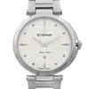 An image of a wristwatch taken from a front close-up angle, focusing on the watch face. The watch is a display model with a silver metallic case and a matching bracelet. The face features a textured pattern radiating from the center, with the brand name "Eterna" and the phrase "Since 1856" visible. The watch includes simple hour markers and a date display at the 6 o'clock position. The crown is adorned with small decorative stones.