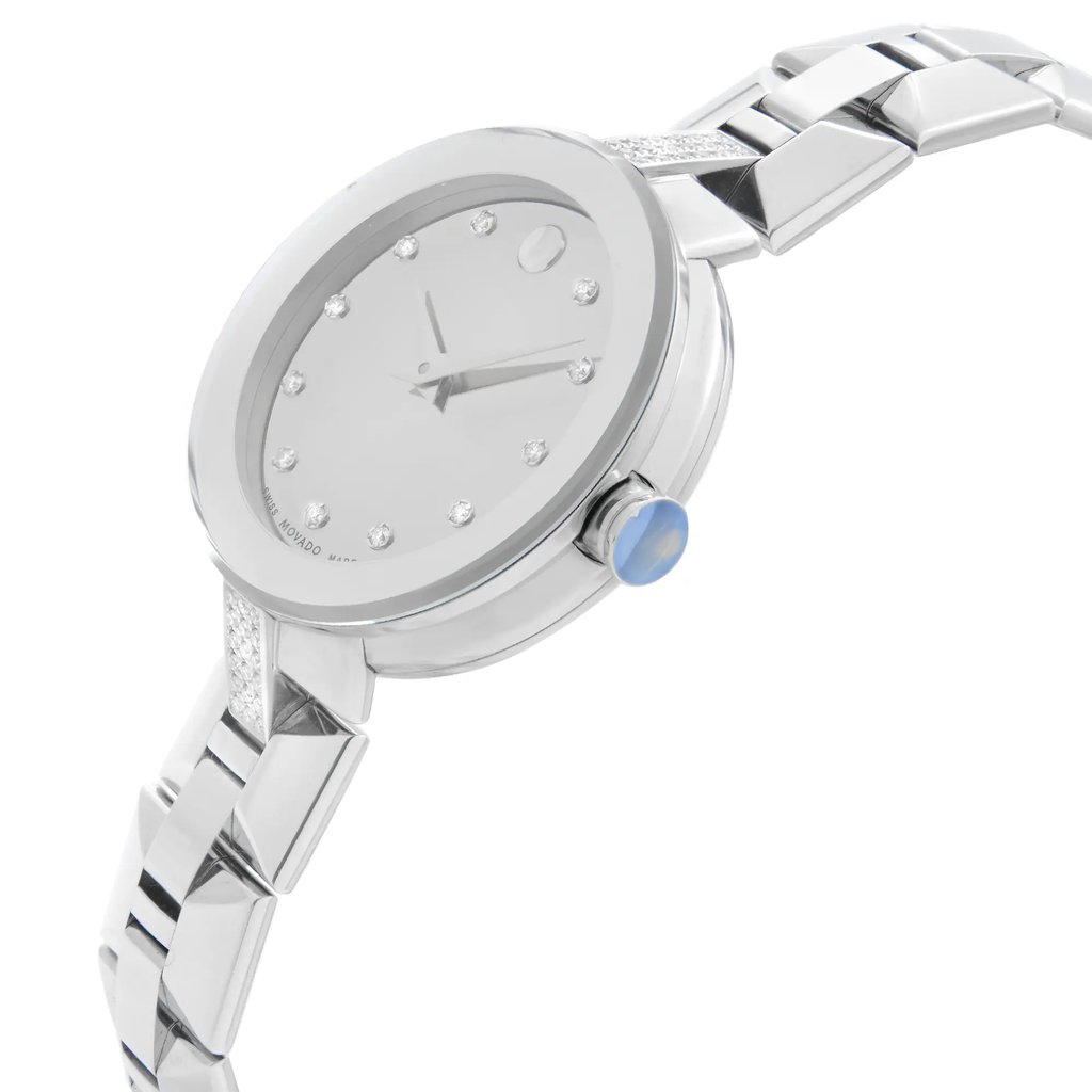 An image of a wristwatch viewed from the side profile, showcasing the crown prominently. The watch is positioned at an angle that highlights its sleek design and metallic finish. The distance is close enough to display intricate details such as the polished links of the bracelet and the minimalist dial with hour markers. The crown features a blue accent, adding a touch of color to the otherwise silver-toned watch. The watch is in display model condition.