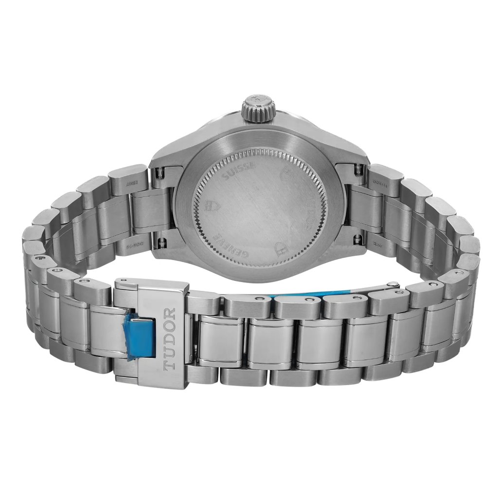 An image of a wristwatch viewed from the back, showing the closed clasp. The watch is positioned centrally, with the camera capturing it from a straight-on angle at a close distance. The metal bracelet and the back of the watch case are clearly visible, highlighting its unworn condition. The brand name "Tudor" is engraved on the clasp.