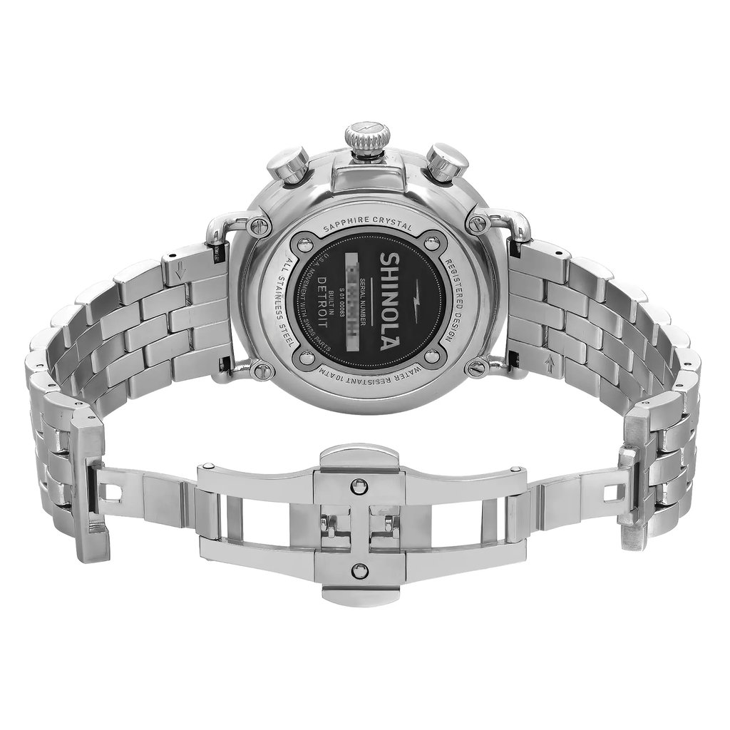 An image of a pre-owned wristwatch showing the back view with an open clasp. The watch is positioned centrally, with the metal bracelet spread out horizontally. The angle is directly from behind, highlighting the back case and the open deployment clasp. The distance is close enough to see details like the brand name "Shinola" and inscriptions on the case.
