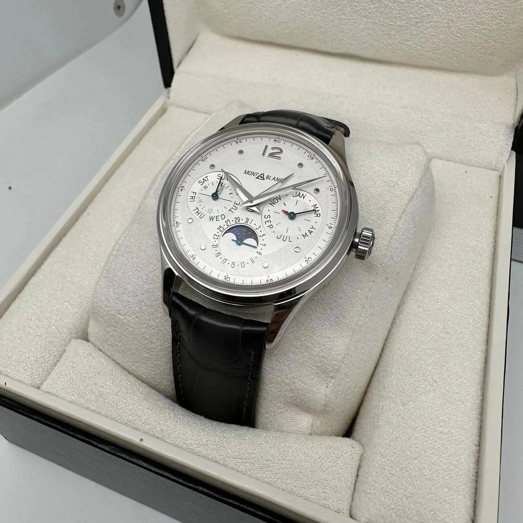 An image of a pre-owned Montblanc men's wristwatch with day/date, GMT, luminous hands, and moon phase features. Positioned at a slight angle, the watch is displayed in full view inside its open box, accompanied by documents. The watch face is visible, and the timepiece rests on the cushioned interior of the box, which fills the frame. The photo is taken from a top-down perspective, at a close distance, showcasing the watch's details clearly.