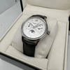 An image of a pre-owned Montblanc men's wristwatch with day/date, GMT, luminous hands, and moon phase features. Positioned at a slight angle, the watch is displayed in full view inside its open box, accompanied by documents. The watch face is visible, and the timepiece rests on the cushioned interior of the box, which fills the frame. The photo is taken from a top-down perspective, at a close distance, showcasing the watch's details clearly.