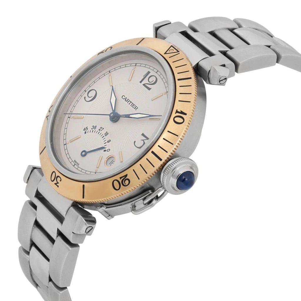 An image of a pre-owned Cartier men's wristwatch, viewed from a slightly elevated angle. The watch features a two-tone design with a stainless steel bracelet and a yellow gold bezel. The face includes a date indicator and luminous hands, with black numerals and indices. The crown is adorned with a blue cabochon. The photo is taken close up, highlighting the intricate details of the watch's design.