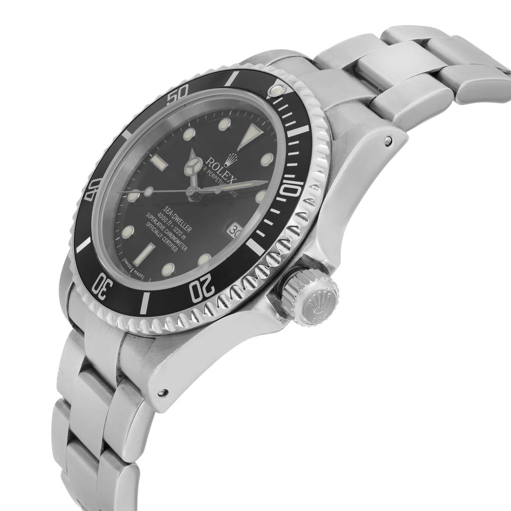 An image of a pre-owned men's Rolex luxury wristwatch viewed from the side profile, showcasing the crown prominently. The watch features a round shape with a black dial and bezel, and is made of stainless steel, indicating good condition. The band is also stainless steel. Notable features include a date indicator and luminous hands.