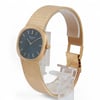 An image of a pre-owned Patek Philippe wristwatch positioned upright on a clear display stand. The watch is viewed from a slightly angled front-left position, showcasing its elegant design. The timepiece features a blue dial with yellow gold hour markers and hands, encased in a gold frame. The textured gold bracelet is partially visible, highlighting its luxurious appearance. The image is taken from a moderate distance, capturing the watch's intricate details and craftsmanship.