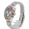 An image of a pre-owned men's Rolex wristwatch, angled slightly from the front and left side, showcasing its stainless steel bracelet and case. The watch features a multicolored bezel, chronograph functionality, luminous hands, and small seconds subdial. The watch is positioned upright on a transparent stand with a close-up view highlighting its intricate details.