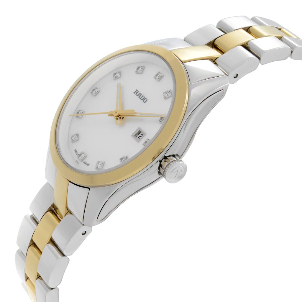 An image of a wristwatch taken from a side profile view. The watch features a silver and gold two-tone metal band. The crown, displaying a logo, is visible on the right side. The watch face is white with gold hour markers, and a date window is present. The angle highlights the watch's sleek design, and it is photographed at a close distance, showcasing its details clearly.