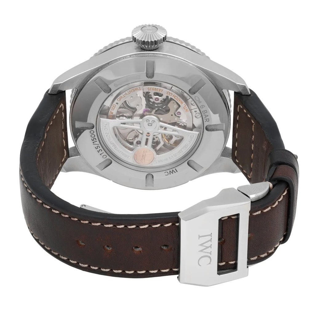 An image of a pre-owned IWC Timezoner Le Petit Prince Edition men's wristwatch viewed from the back at a slight angle, showcasing the intricate mechanism through the transparent case back. The watch features a silver metal case, a dark brown leather strap with white stitching, and a metal clasp engraved with "IWC." The image is taken at a close distance, highlighting the detailed craftsmanship and the watch's luminous hands feature.
