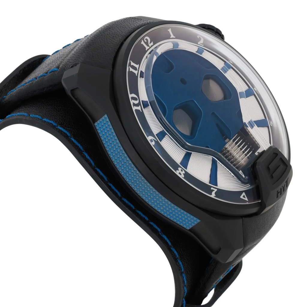 An image of a pre-owned HYT Skull AXL Guns N Roses 51mm Titanium PVD men's wristwatch, viewed from a low angle and close-up. The watch features a black case with blue accents and a unique blue dial design. The hour markers are prominent around the edge, set against a blue and silver background. The strap is black with blue stitching, complementing the watch's color scheme.
