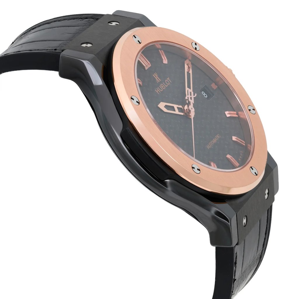An image of a pre-owned men's Hublot wristwatch, viewed from a side angle. The watch features a black strap and a rose gold bezel with visible screws. The face of the watch is dark with rose gold hour markers and hands, and includes a date indicator. The angle shows the watch at a slight tilt, highlighting the thickness of the case and the texture of the strap, captured from a close distance.