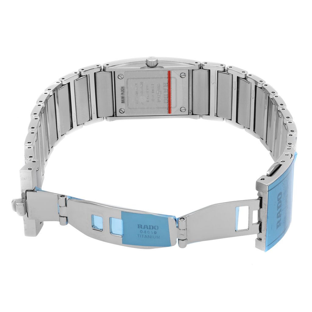 An image of a wristwatch taken from the back view, showcasing the open clasp. The watch is positioned horizontally, highlighting the titanium links and the clasp mechanism. The brand name is visible on the clasp, which is partially covered by blue protective film. The image is taken at a close distance, emphasizing the details and craftsmanship of the watch. The condition is noted as new with defects.