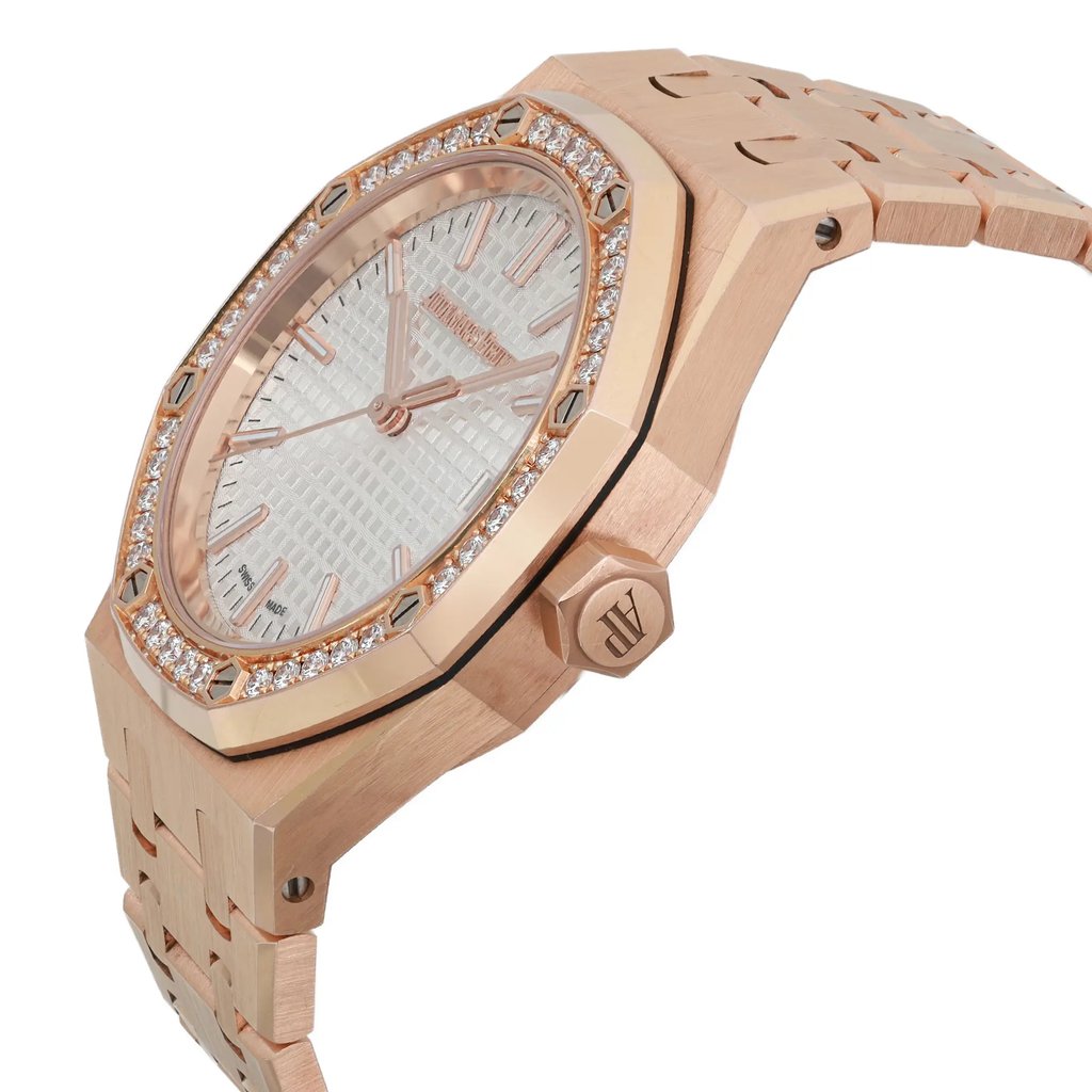 An image of a pre-owned Audemars Piguet men's luxury wristwatch, viewed from the side profile at a slight angle, showcasing the crown. The watch features a distinctive octagonal shape, with a rose gold bezel and band. The dial is silver with a "Tapisserie" pattern and luminous hands, framed by a rose gold bezel adorned with diamonds. The overall condition is classified as good.