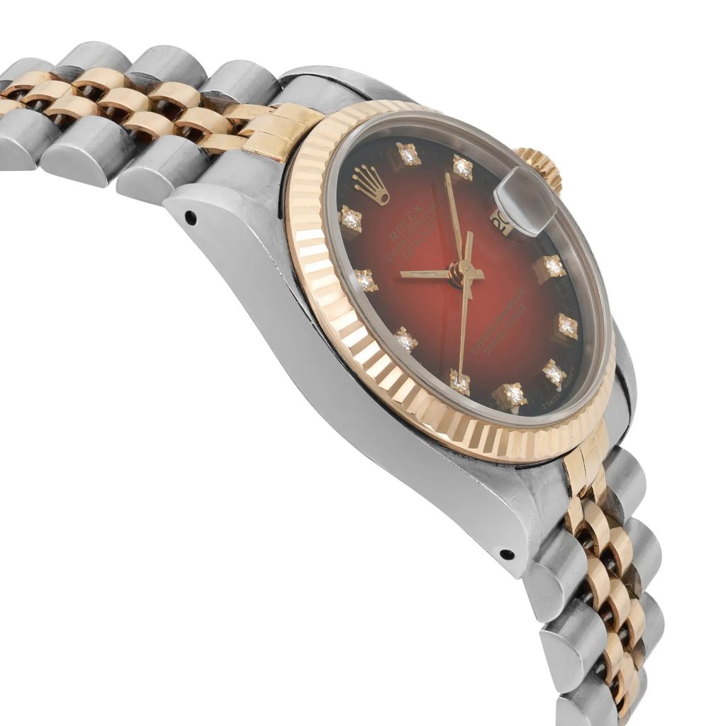 An image of a pre-owned wristwatch shown from a side profile view, opposite the crown. The angle highlights the watch's fluted bezel and the intricate design of its two-tone metal bracelet. The watch face is partially visible, displaying a red gradient color with diamond hour markers. The focus is on the watch case and bracelet at a close distance, showcasing its luxurious details.