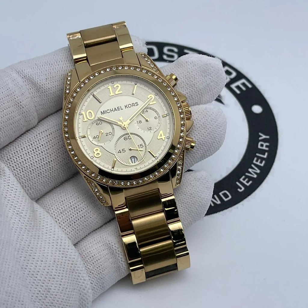 An image of a Wristwatch by Michael Kors. This Pre Owned item is designed for Women, featuring a Dress/Formal style. It has a Quartz movement and an Analog display with a Gold dial color. The indices include 12-Hour Dial,Arabic Numerals,Multi Dial,Non-Numeric Hour Marks,Seconds Hand. The band is made of Stainless Steel and the case is made of Stainless Steel. The watch has a Round shape with a case size of 39 mm and a case thickness of 11.5 mm.