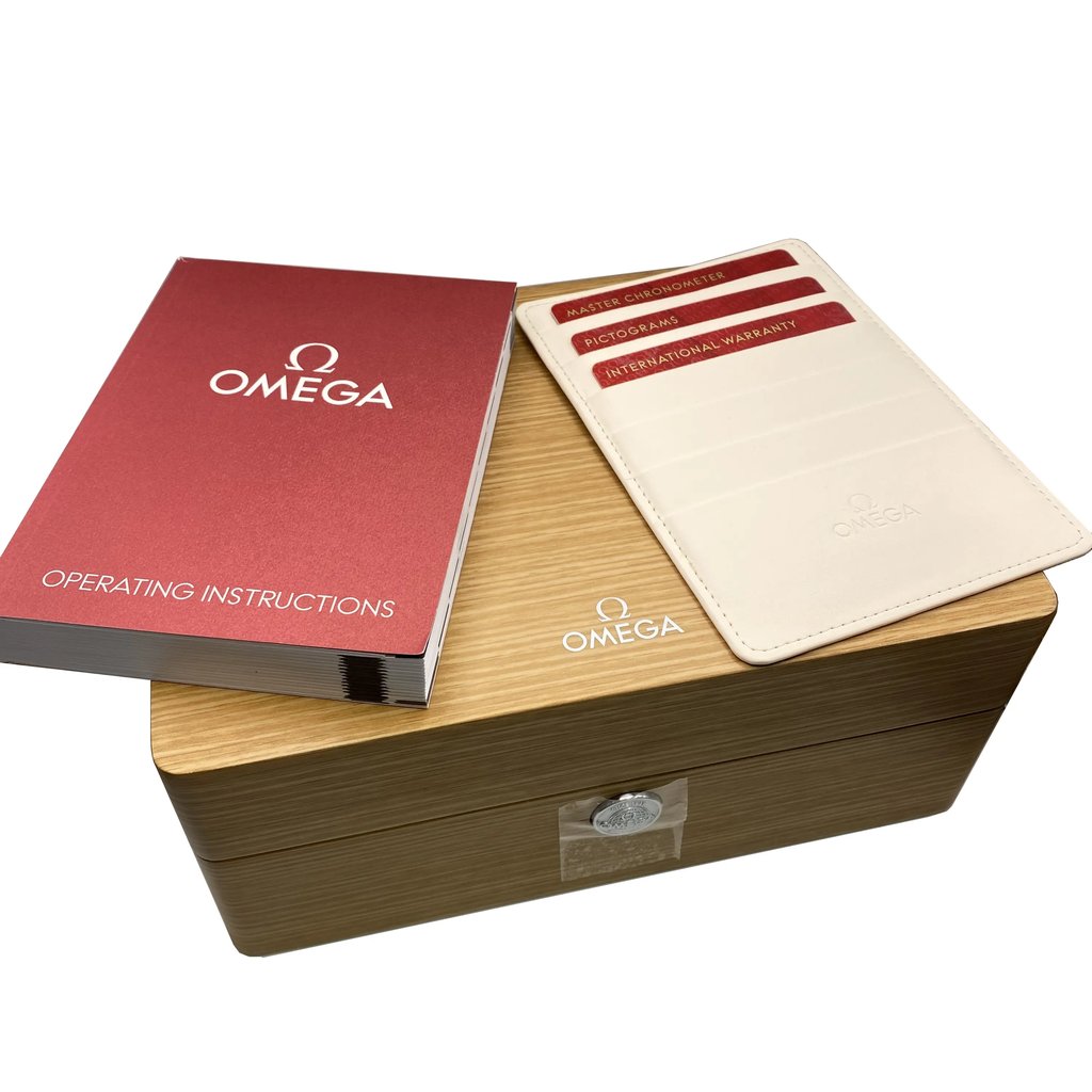 An image of a wristwatch's packaging and documentation, viewed from a slightly elevated angle. The wooden box is centered, with the brand's logo visible on top. To the left, a red operating instructions booklet is placed at an angle. On the right, a white cardholder containing multiple cards is partially visible. The image captures the items at close range, emphasizing the new condition of the packaging materials.