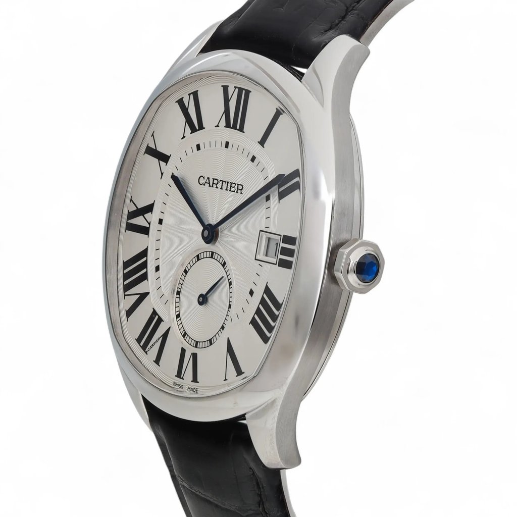 An image of a pre-owned Cartier men's wristwatch taken from a slight side angle, showcasing its elegant silver case and black leather strap. The watch features a white dial with bold Roman numerals and a date indicator at the 3 o'clock position. The blue sapphire crown is prominently visible on the right side of the case. The image is taken from a medium distance, highlighting the watch's sophisticated design details.