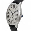 An image of a pre-owned Cartier men's wristwatch taken from a slight side angle, showcasing its elegant silver case and black leather strap. The watch features a white dial with bold Roman numerals and a date indicator at the 3 o'clock position. The blue sapphire crown is prominently visible on the right side of the case. The image is taken from a medium distance, highlighting the watch's sophisticated design details.