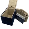An image of a Breitling men's wristwatch packaging, without the watch present. The view is from a slightly elevated angle, showing the full open box and documents. The box is navy blue with a beige interior, and the Breitling logo is embossed on the lid's interior. The box is positioned to the left and angled to show the interior clearly. To the right, there is a beige cushion for the watch, and a warranty card holder with documents partially visible, both bearing the Breitling logo. The items are in the foreground and occupy most of the frame, suggesting a close-up perspective. 