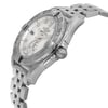 An image of an unworn Breitling women's luxury wristwatch with a side profile view that prominently displays the watch crown. The stainless steel case has a round shape and features a protective sticker, highlighting its pristine condition. The watch has a white mother of pearl dial pattern, luminous hands, and a date indicator, set within a gray bezel. The band is made of stainless steel and the watch is photographed at a close distance, ensuring the details are clearly visible.