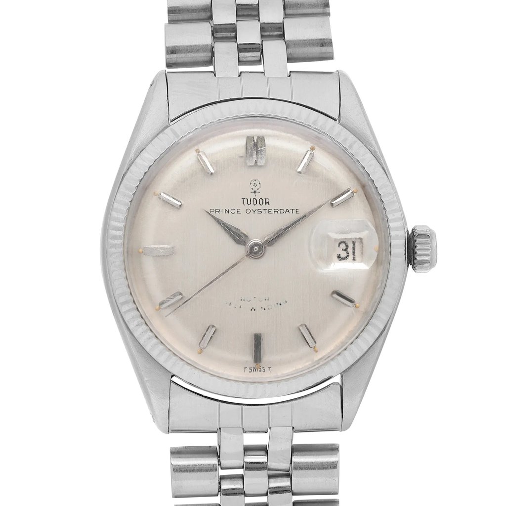 An image of a pre-owned Tudor men's wristwatch positioned upright, showing a front-facing view. The watch features a silver dial with a date indicator at the 3 o'clock position. The white gold bracelet and the watch's crown are visible, highlighting its classic design. The angle and proximity provide a clear, detailed look at the watch face and its features.