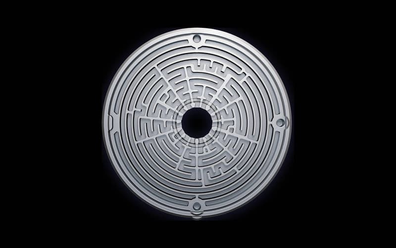 Kreisrunde, labyrinthartige MAT-Scheibe aus Metall mit Öffnung in der Mitte, Draufsicht auf schwarzem Hintergrund