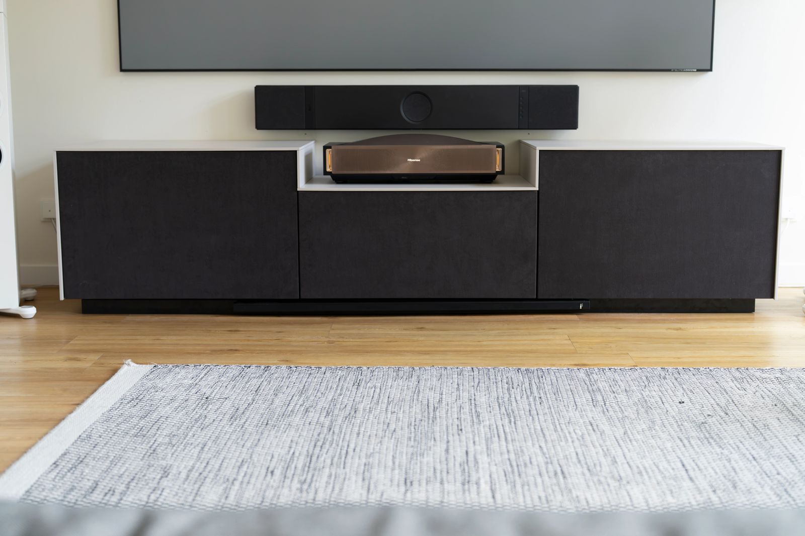 LaserBoard V1 in Dunkelgrau mit drei geschlossenen Fronten, in der Mitte die tiefer gesetzte helle Ablage mit einem Laser TV, darüber Soundbar und Leinwand