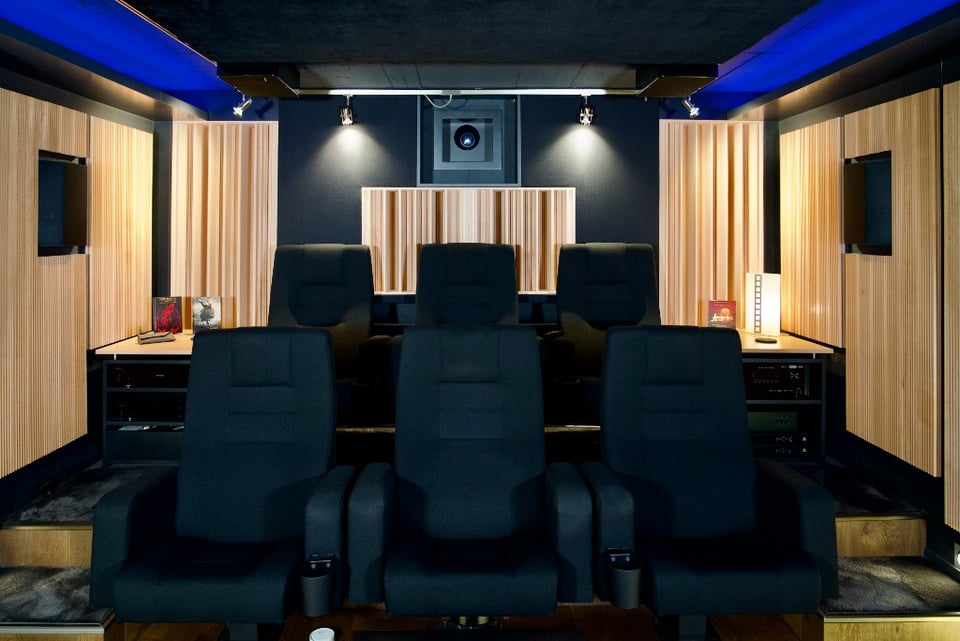 Black Cinema mit Holzlamellen-Akustikpaneelen an den Wänden und dunklen Kinosesseln, AVITECT-Referenzprojekt