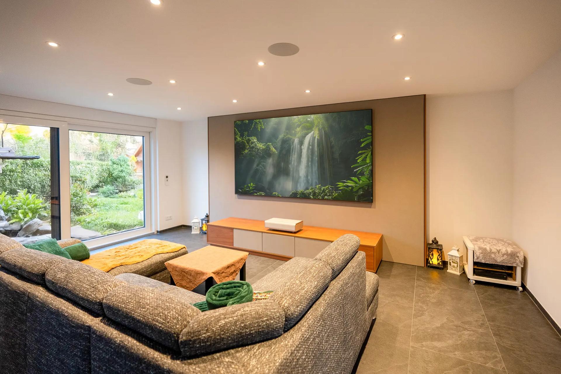 Wohnzimmer mit Holz-Lowboard vor einer Wandverkleidung, darüber die Leinwand mit laufendem Bild; Laser-TV-Projekt aus dem AVITECT-Lookbook