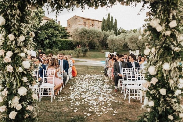 Castello di Montignano, Massa Martana — a white-rose ceremony arch framing the petal-strewn aisle at an Umbrian castle wedding