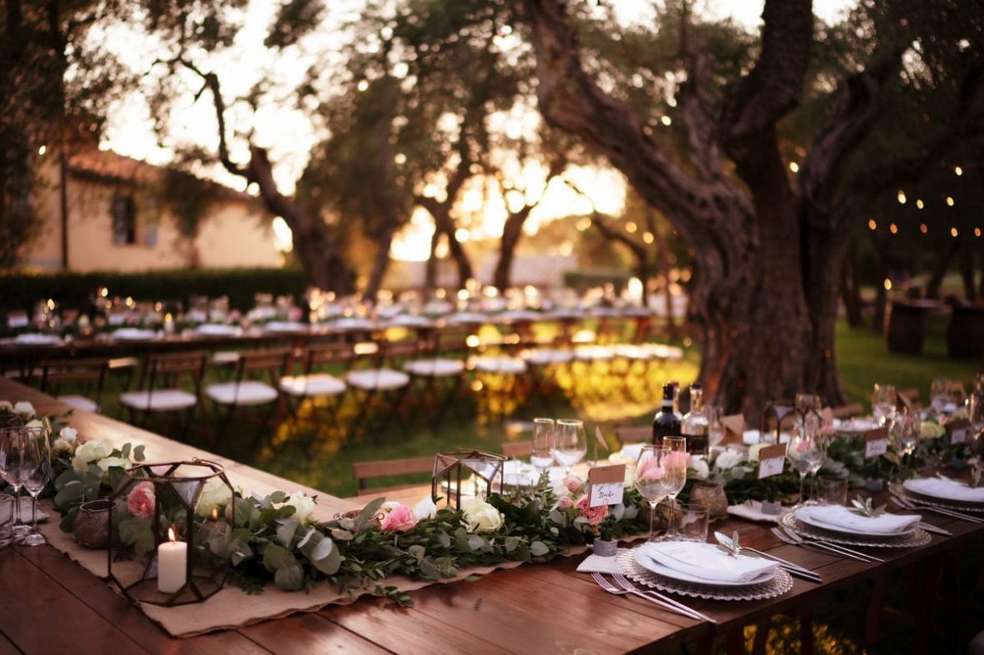 Terre di Nano, Pienza — wedding tables dressed with greenery and candles under old olive trees at sunset