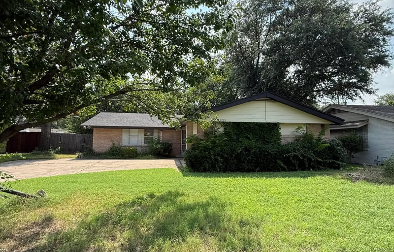 Single-story brick home with an attached garage set behind a large shade tree in Irving, Texas