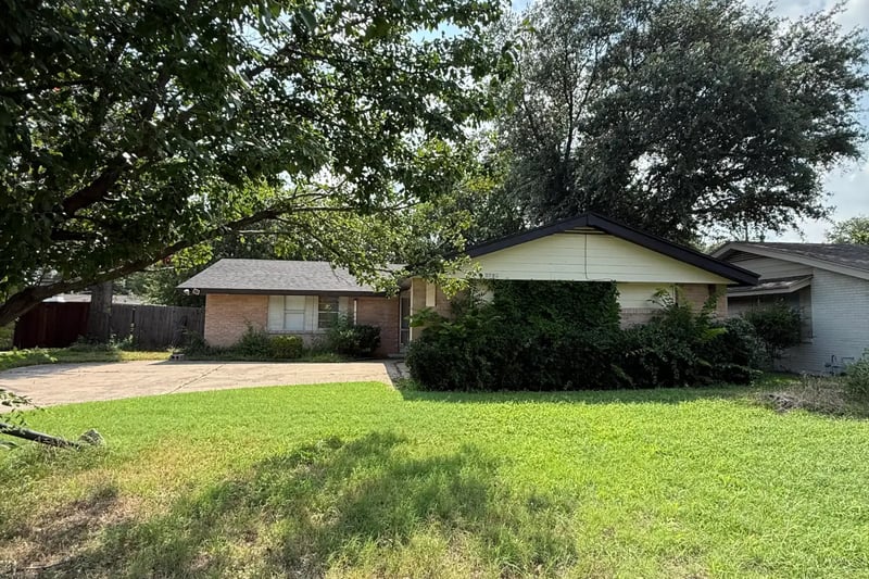 Single-story brick home with an attached garage set behind a large shade tree in Irving, Texas