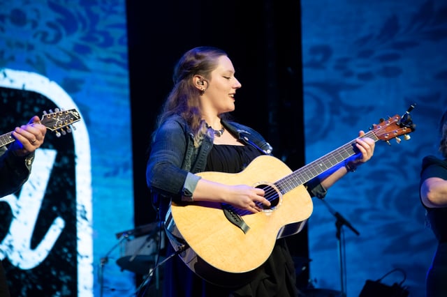 Jessica Dutton singing and playing acoustic guitar in front of a Bluegrassified backdrop