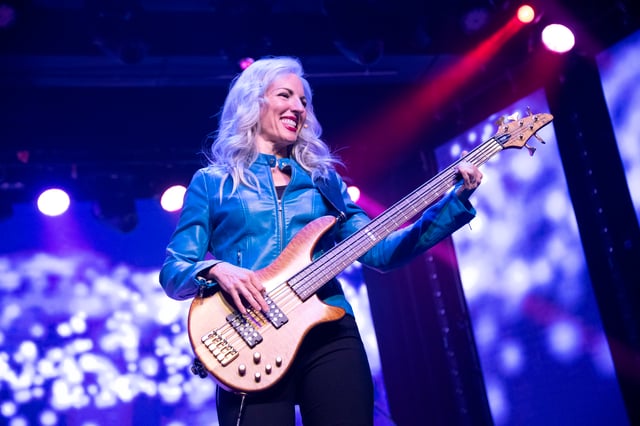 Evette Dutton playing electric bass in a blue leather jacket