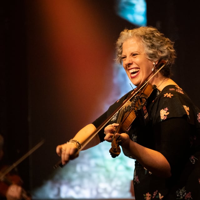 Amy Dutton Arambulo laughing as she plays the violin