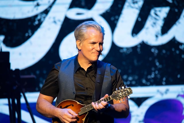 Timothy Dutton playing mandolin in front of the Bluegrassified sign