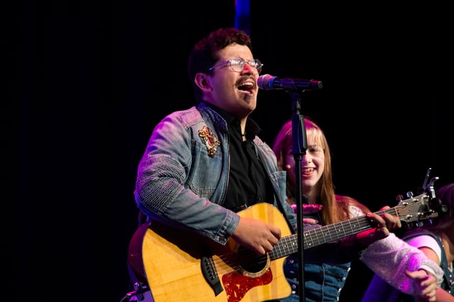 Gabriel Arambulo singing and playing acoustic guitar in a denim jacket