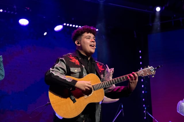 Julian Arambulo singing and playing acoustic guitar in a western shirt