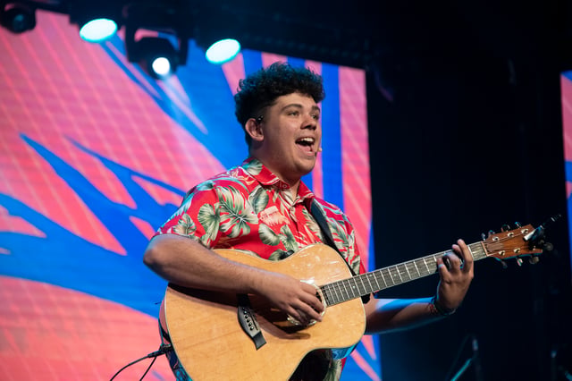 Julian Arambulo laughing as he plays acoustic guitar in a Hawaiian shirt