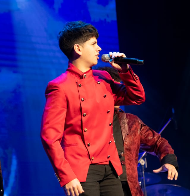 Josiah Arambulo singing in a red military-style jacket