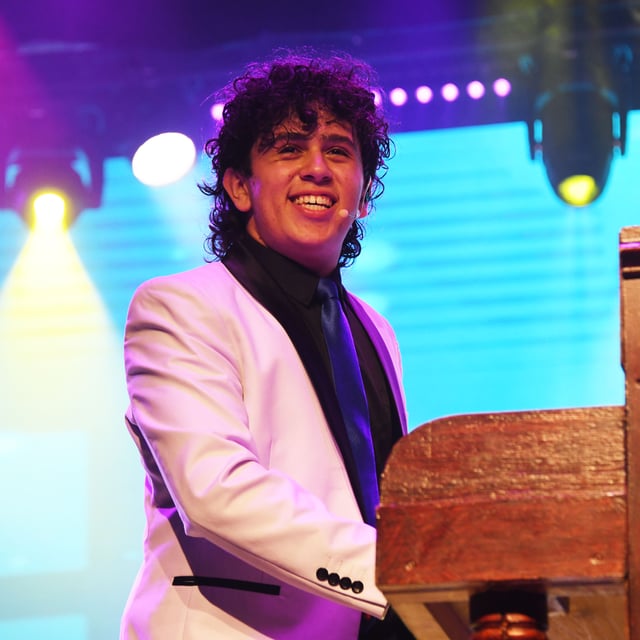 Damian Arambulo smiling at the piano in a white jacket