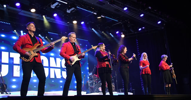 The Duttons in red performing in a line in front of the DUTTONS sign